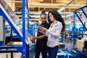 Two women in a manufacturing plant reviewing data on a tablet.