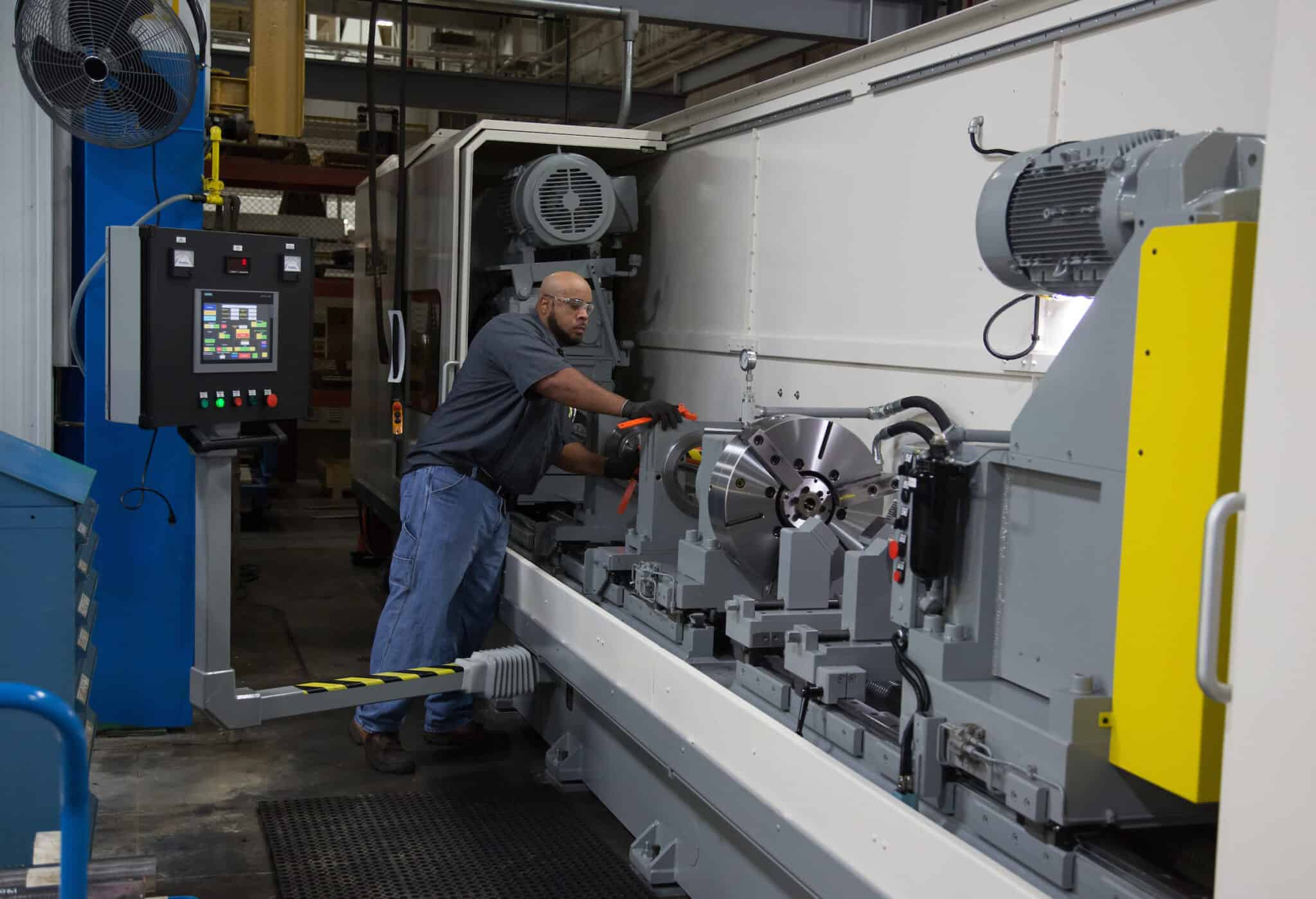 Industrial manufacturing worker operating a large CNC machine in a factory setting.